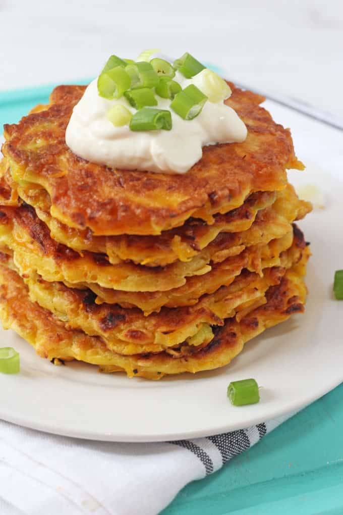Butternut Squash Fritters stacked on a white plate with a dollop of creme fraiche on top and garnished with chopped spring onion.