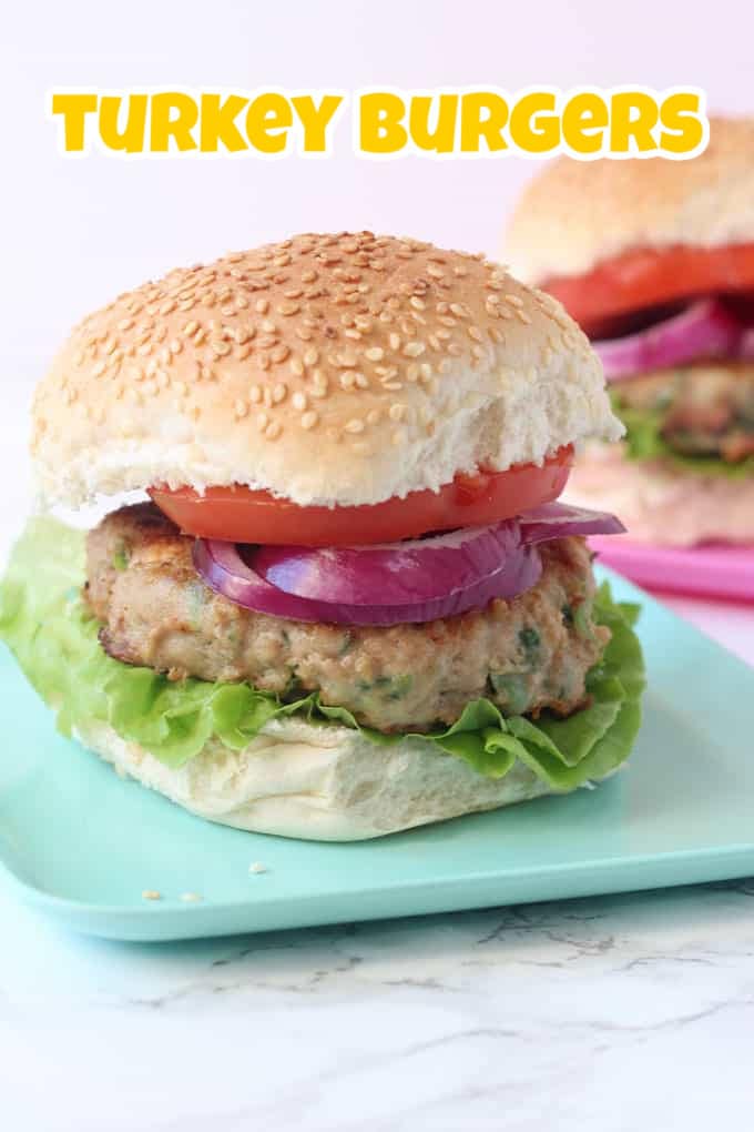 A turkley burger in a seeded bun with lettuce leaves, and sliced tomato and onions.