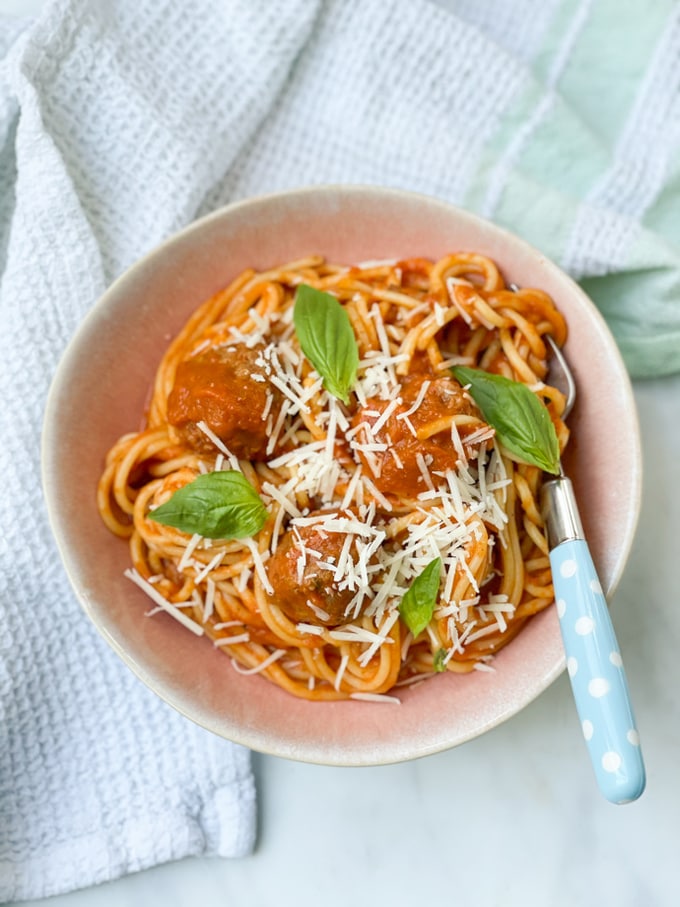 Slow Cooker Spaghetti Meatballs topped with fresh whole basil leaves and finely grated parmesan cheese.