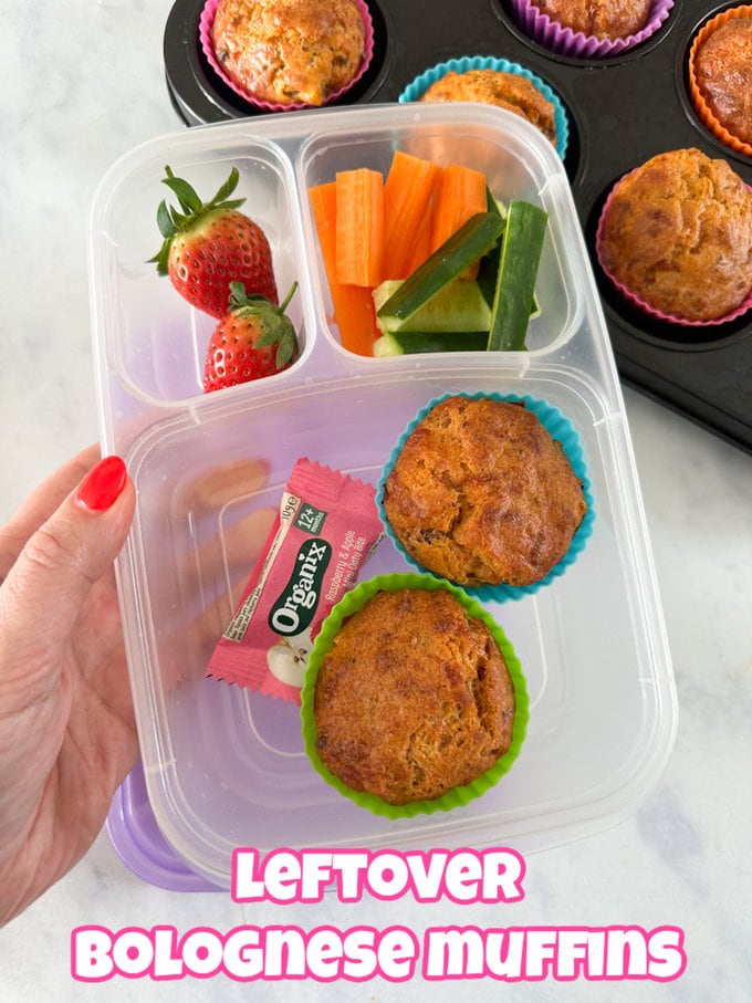 two left over bolognese muffins presented in a clear plastic divided lunch box, served with fresh,chopped veggies and strawberries.